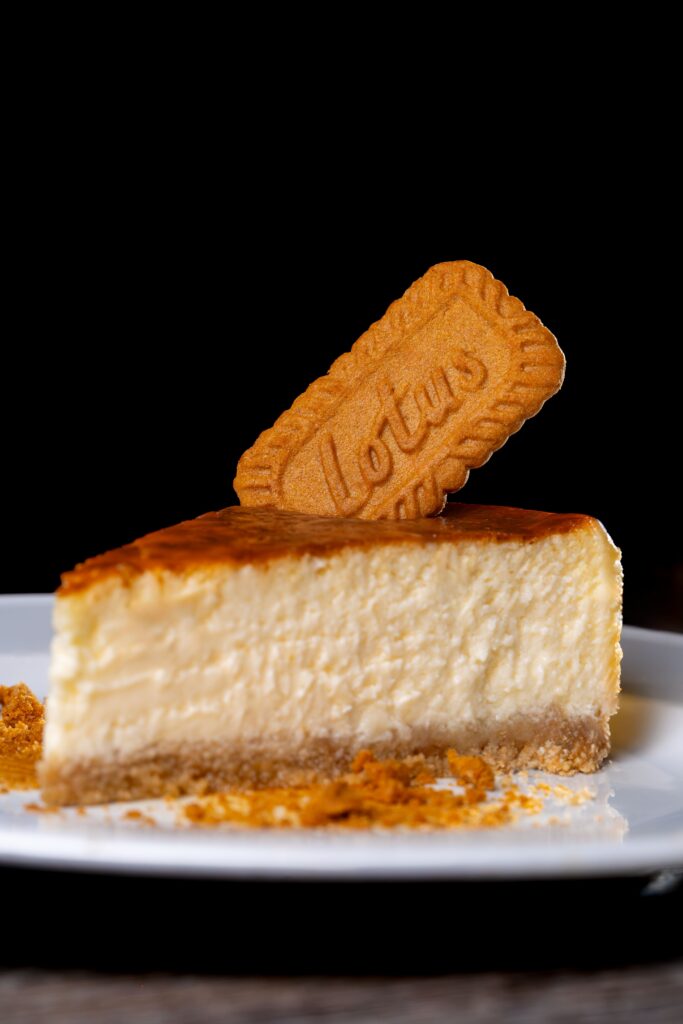 Slice of creamy cheesecake with a Lotus Biscoff biscuit topper on a white plate.