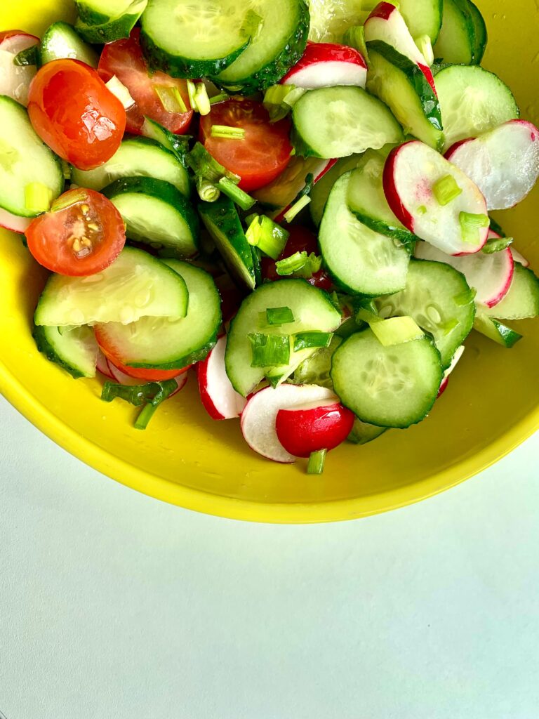 Bright and colorful vegetable salad with cucumbers, tomatoes, and radishes in a yellow bowl.