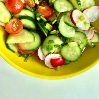 Bright and colorful vegetable salad with cucumbers, tomatoes, and radishes in a yellow bowl.